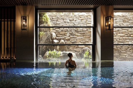 A person in a pool with a stone wall and plants in the background.