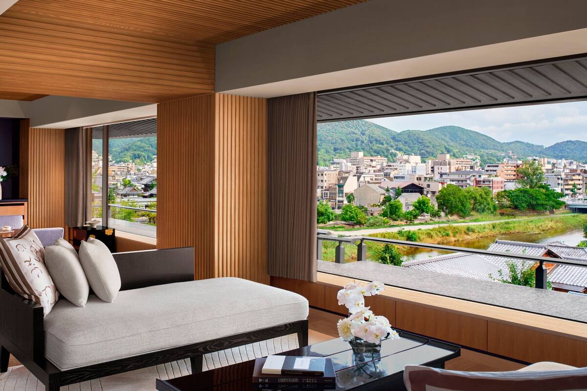 A modern room with a sofa, a glass table, and a view of a cityscape and mountains.