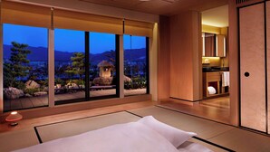 A hotel room with tatami flooring, a bed with white bedding, a view of a garden and mountains, and a traditional Japanese-style interior. - The Ritz-Carlton, Kyoto (Kyoto)