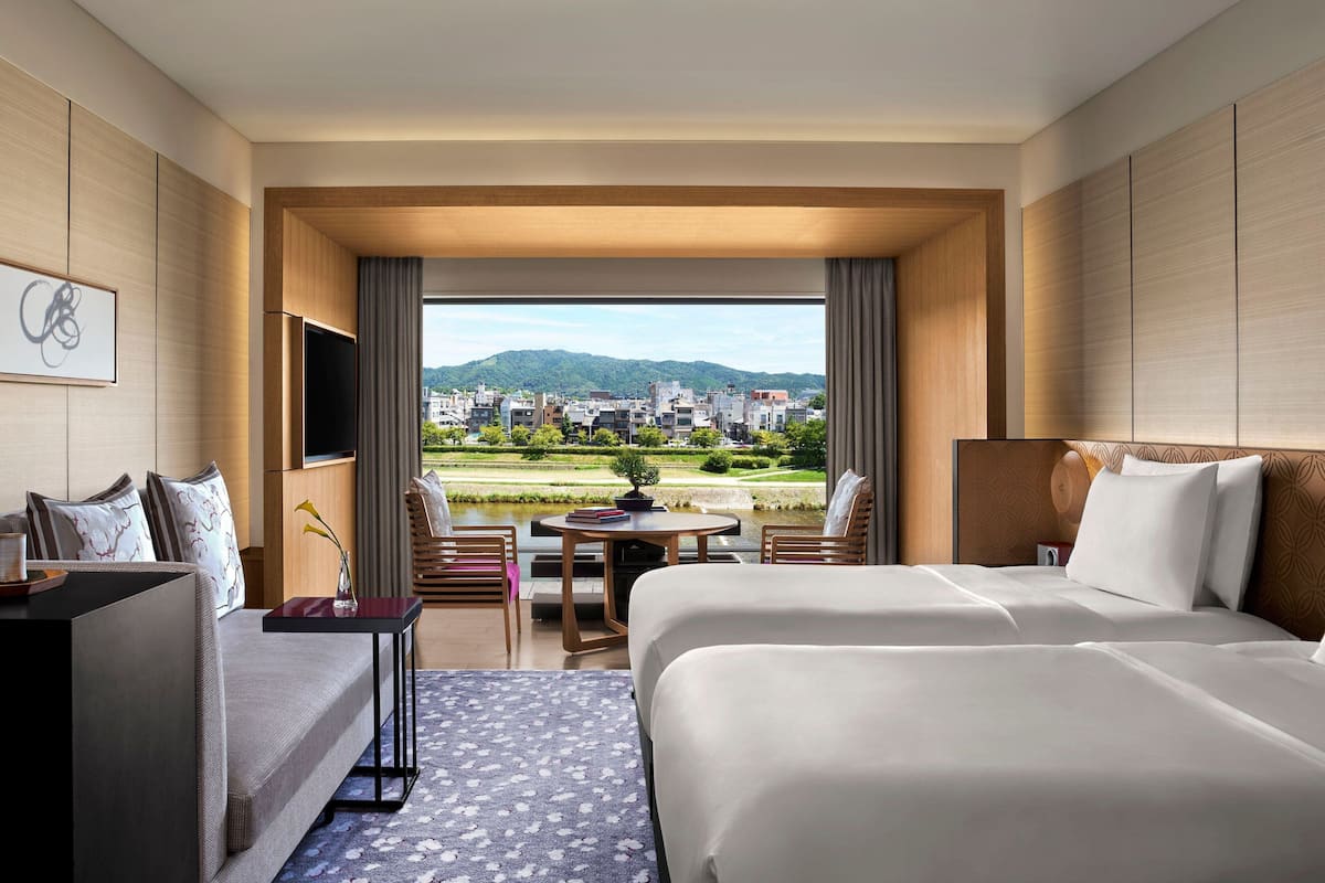A hotel room with a large bed, a sofa, a small table with a plant, and a view of a cityscape and mountains.