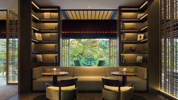 A modern interior with a sofa and two chairs facing a large window, surrounded by bookshelves and a decorative ceiling.