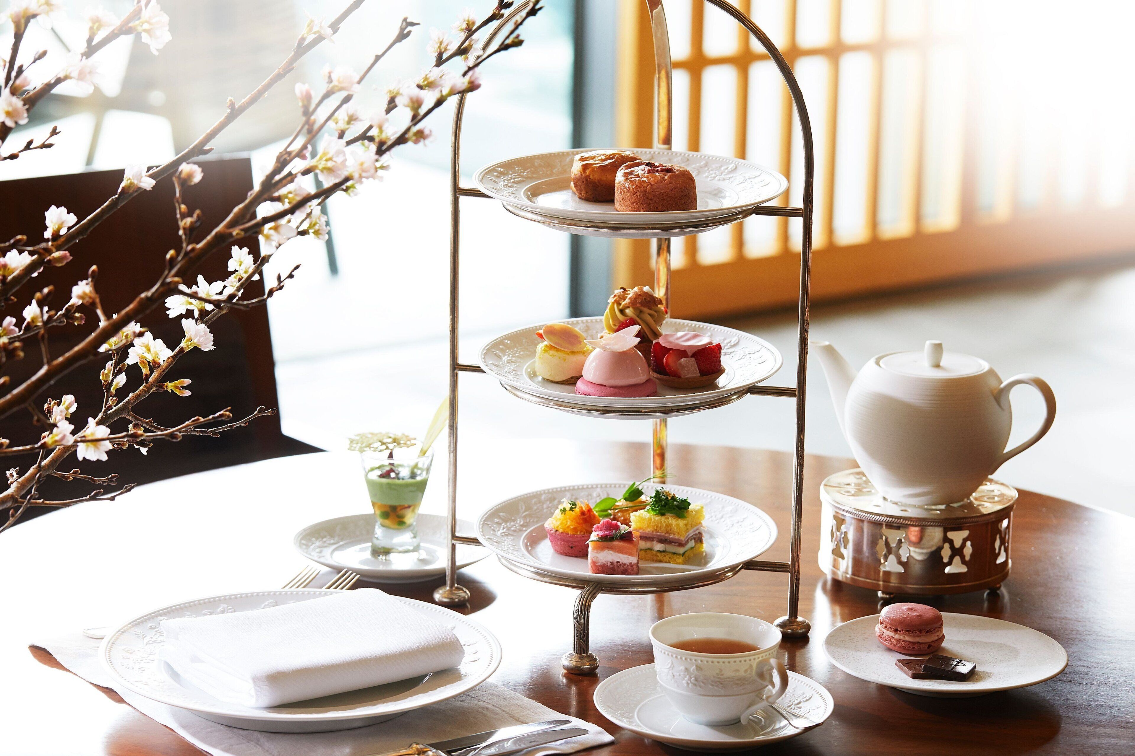 A three-tiered dessert stand with various pastries and a teapot on a table.