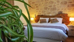 Ein Schlafzimmer mit Steinwand, einem Holzkopfteil, einem Bett mit weißer Bettwäsche, zwei Nachttischlampen und einer grünen Pflanze im Vordergrund.