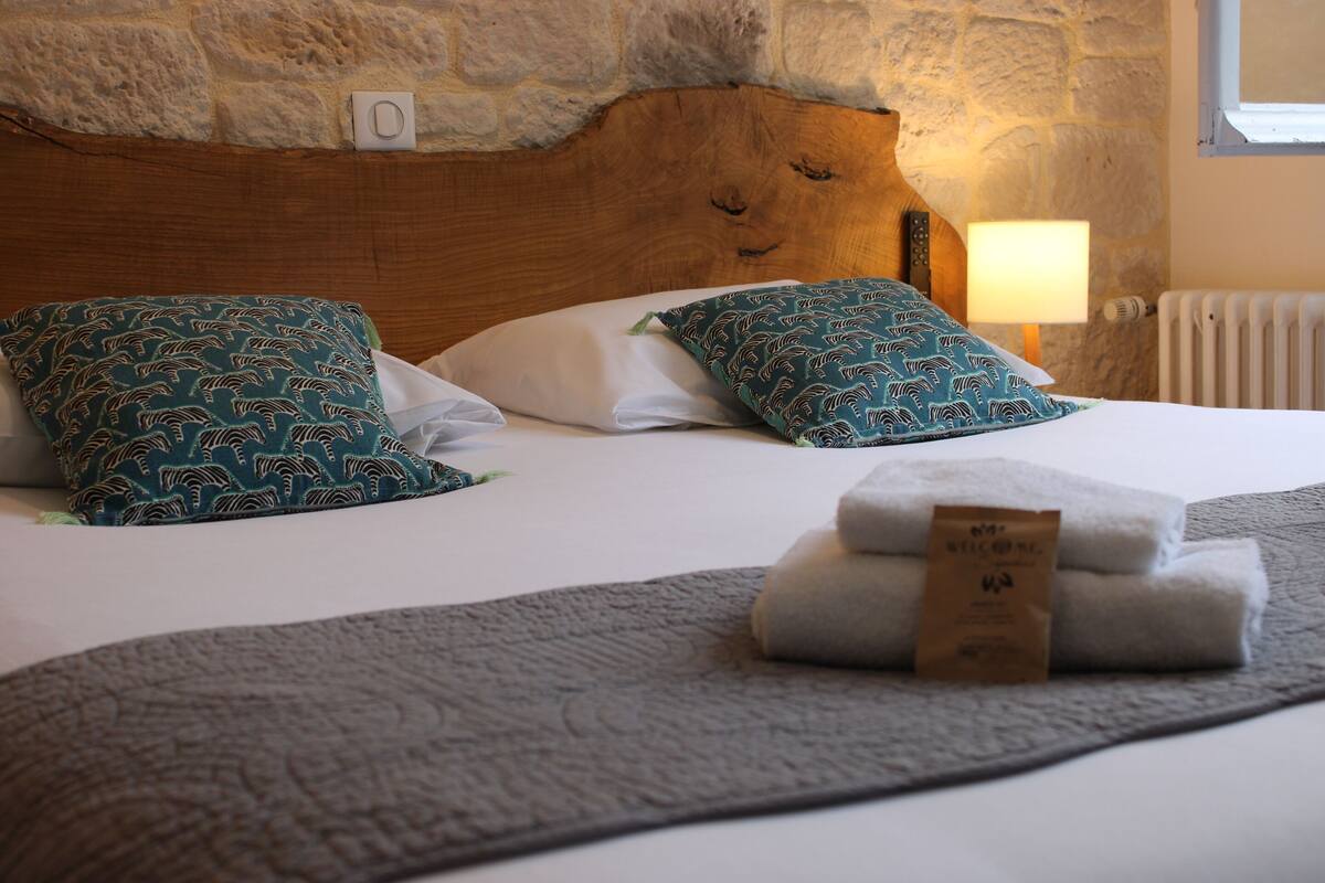 Un lit bien fait, agrémenté d’oreillers à motifs, une serviette pliée et une tête de lit en bois.