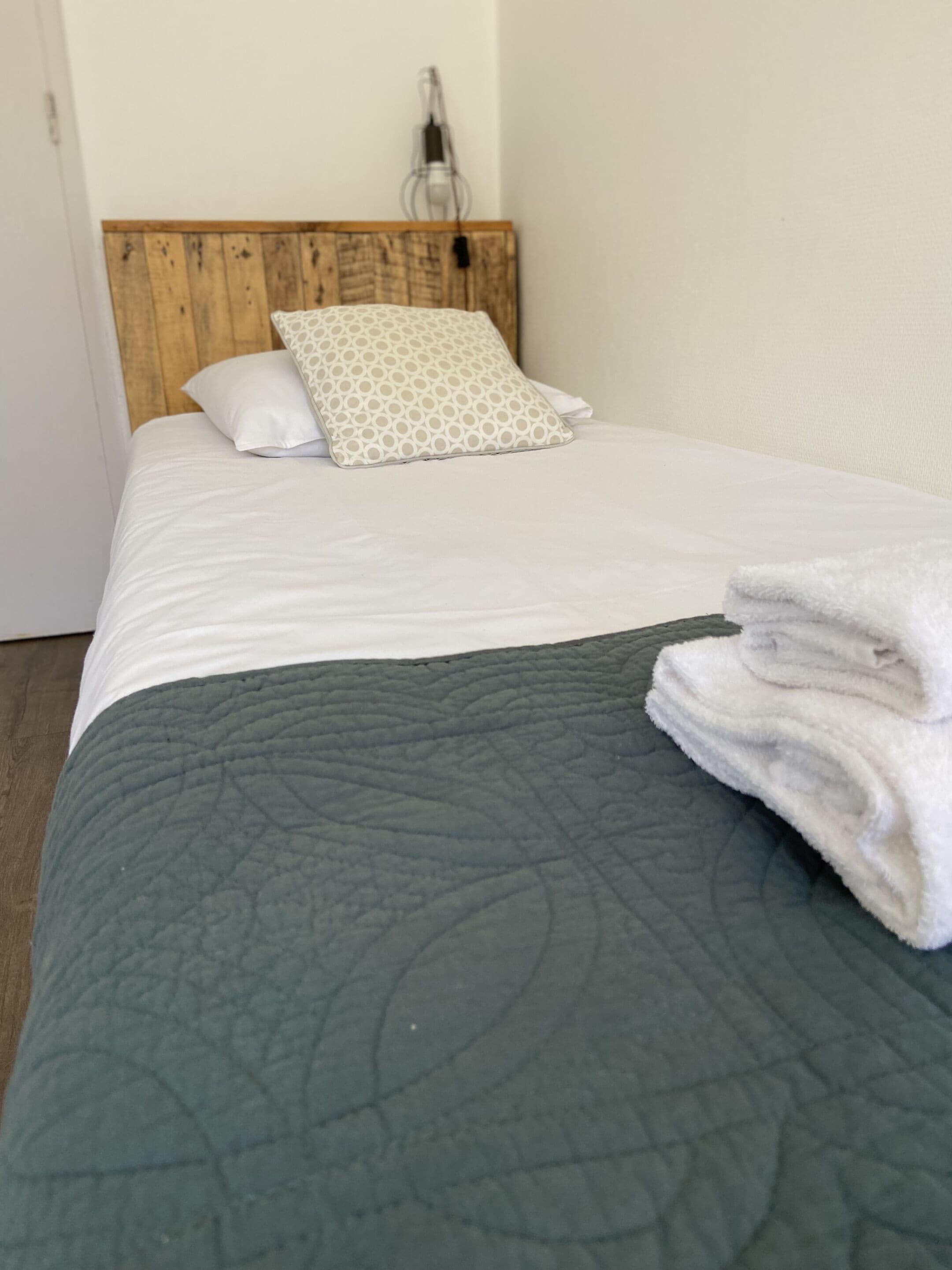 A neatly made bed with a grey quilt, a wooden headboard, and a patterned pillow.
