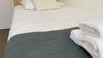 A neatly made bed with a grey quilt, a wooden headboard, and a patterned pillow.