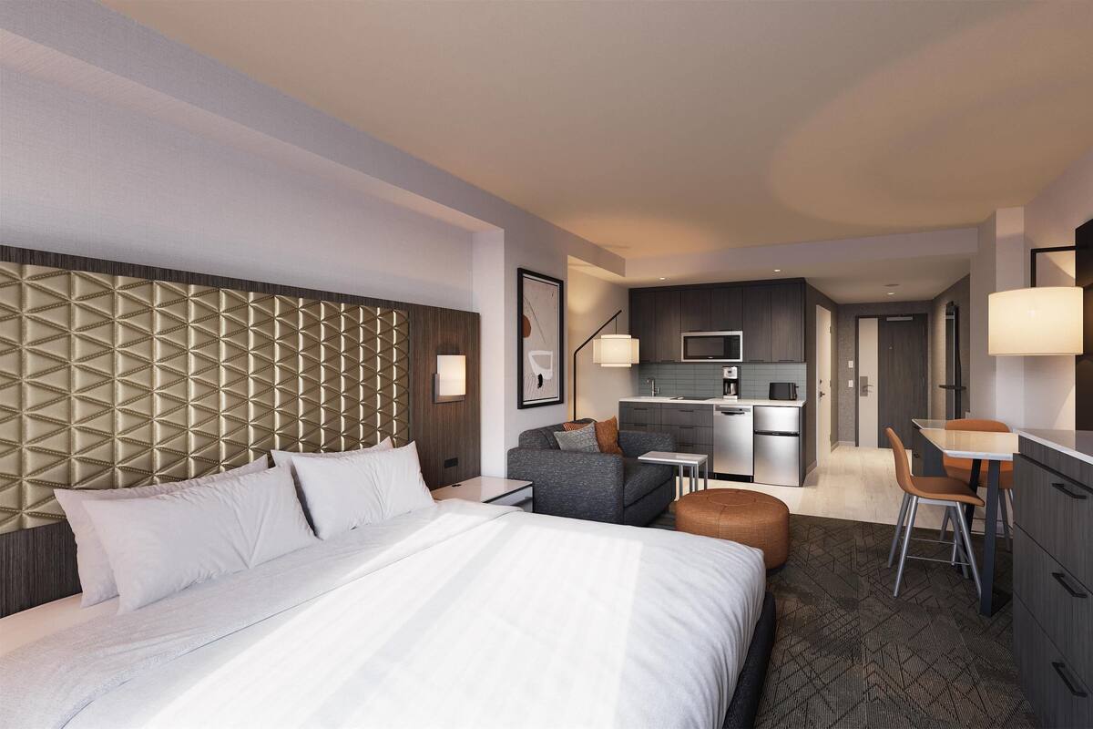 A hotel room with a large bed, a sofa, a desk, a chair, a kitchenette, and a bathroom.
