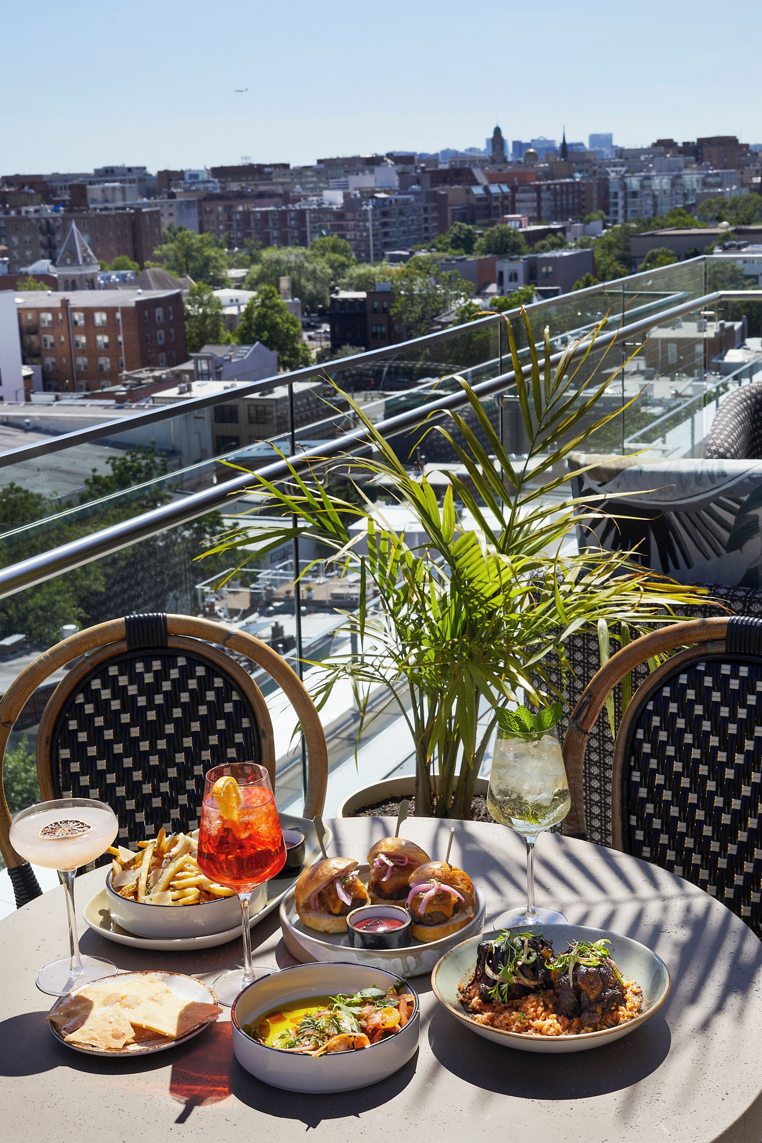 Una mesa de comedor con diversos platos, una copa de vino y vistas a un paisaje urbano.