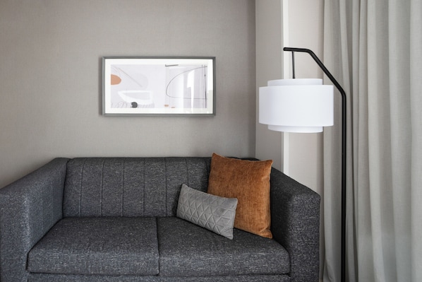 Un canapé gris avec un coussin, une œuvre d’art abstraite encadrée accrochée au mur et une lampe sur pied.
