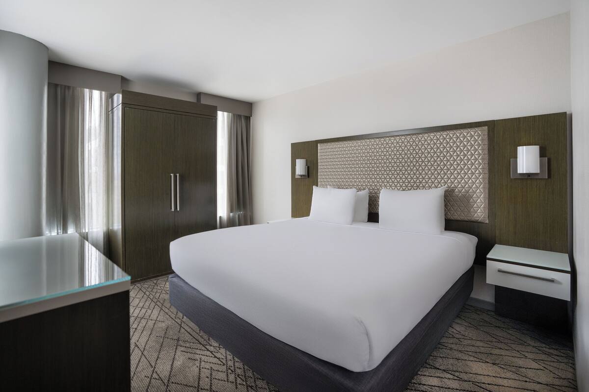 A hotel room with a large bed, a bedside table, a wardrobe, and a glass partition.