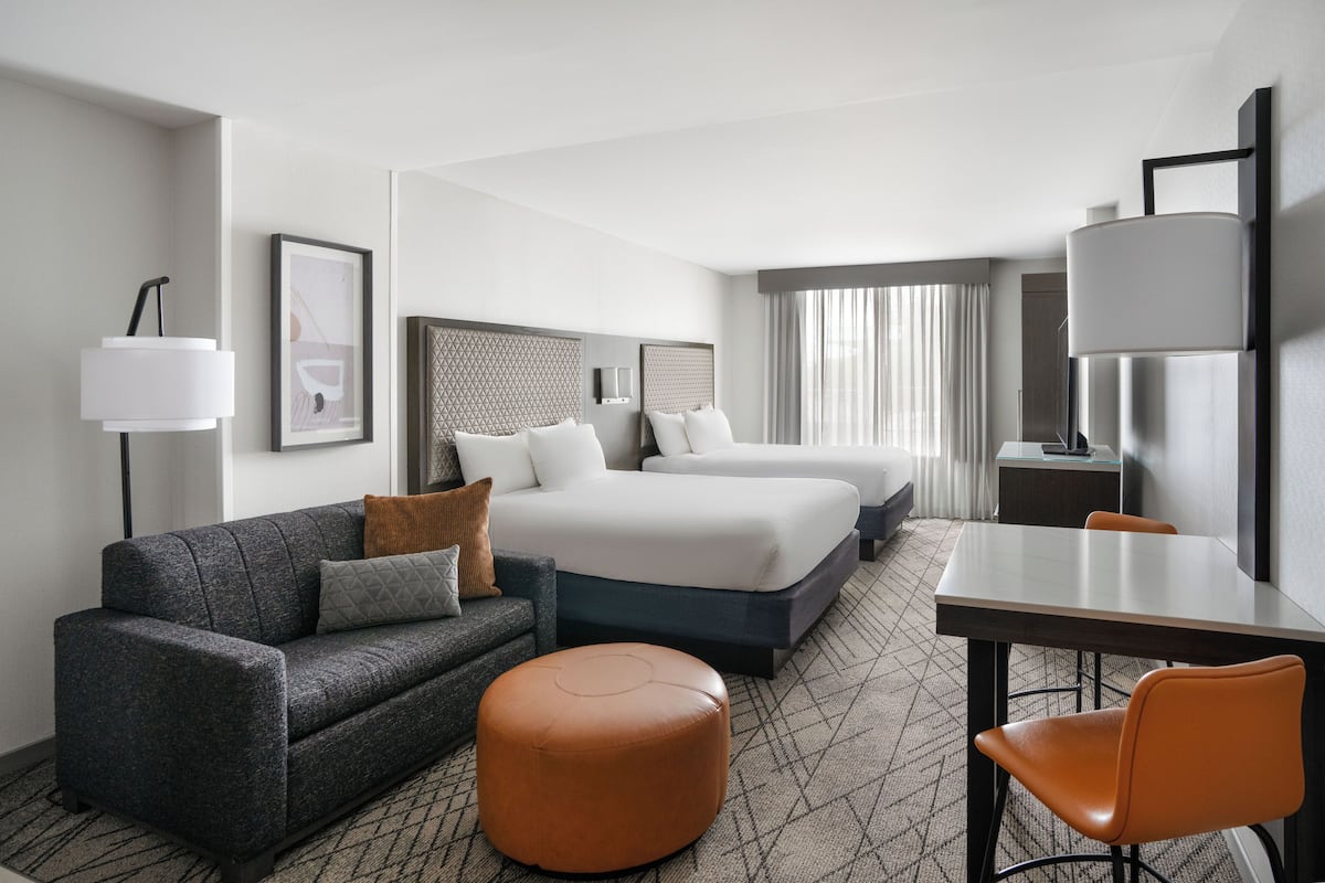 A hotel room with a sofa, two beds, a table, and a chair.