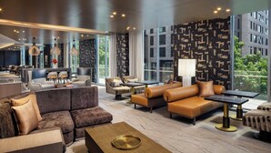 A modern hotel lobby with a sectional sofa, armchairs, a dining area, and a large window offering a city view. - Hyatt House Washington DC / Downtown / Convention Center (Washington)