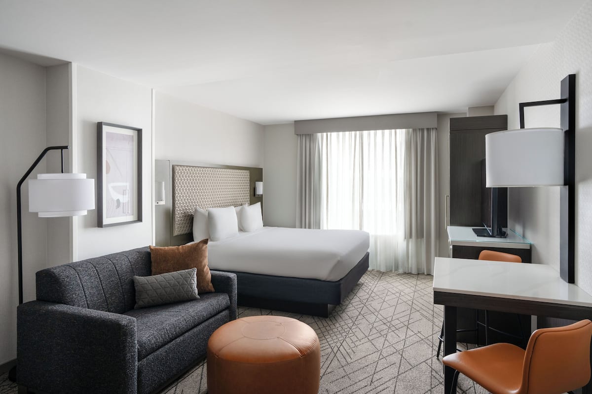 A hotel room with a bed, a desk, a chair, a sofa, and a lamp.