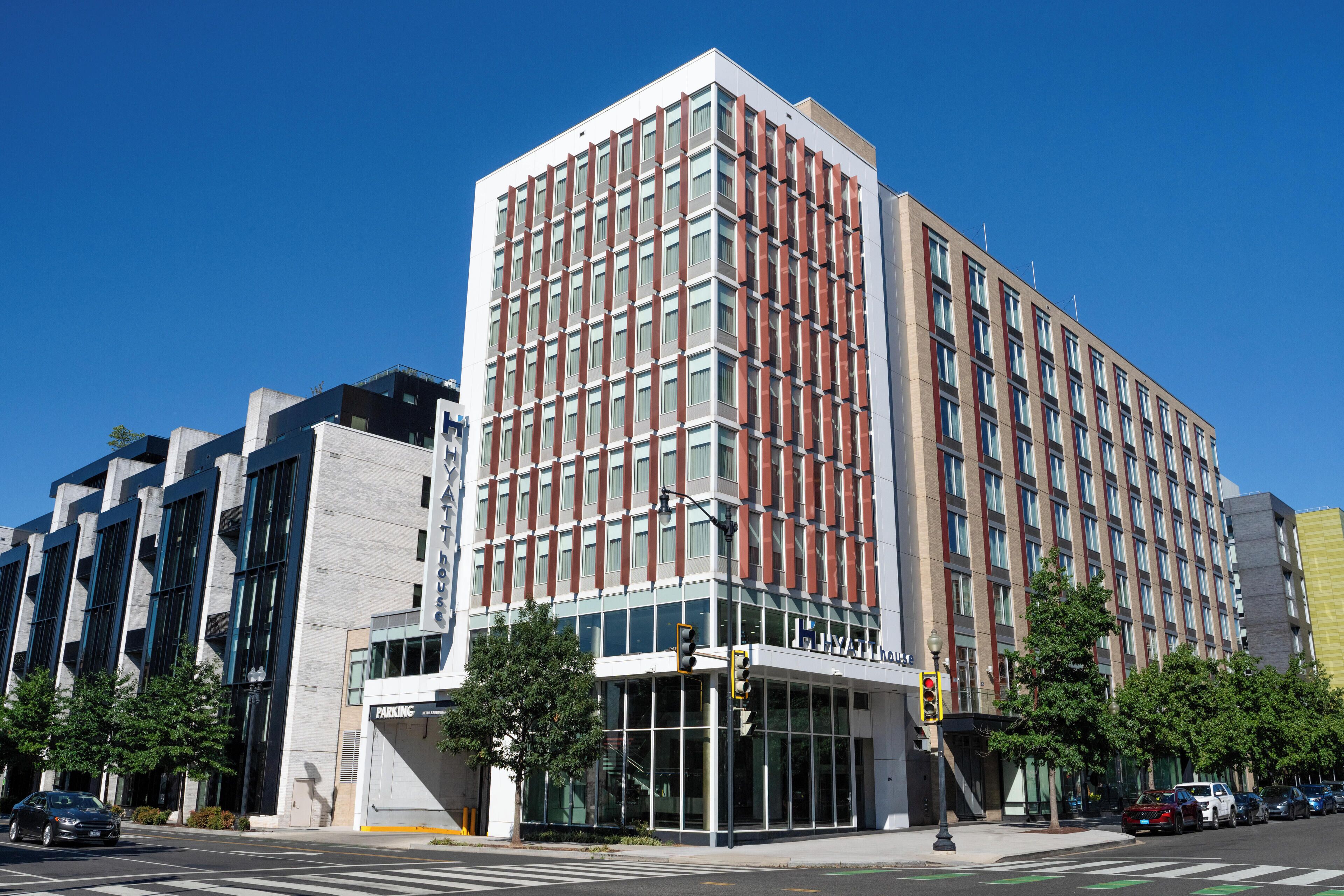 A modern hotel with a glass facade, a parking garage, and a clear blue sky.