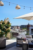 A rooftop terrace with outdoor furniture, a decorative plant, and a view of the cityscape.