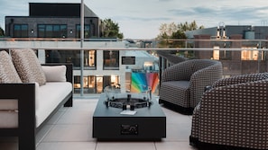 Una terraza en la azotea con un sofá, sillas estampadas, una mesa con un altavoz y vistas a edificios.