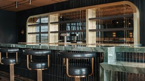 A bar area with a counter, stools, and a view of the kitchen through a window.