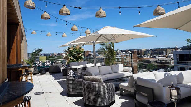 An outdoor seating area with multiple couches, tables, and umbrellas, overlooking a cityscape. - Hyatt House Washington DC / Downtown / Convention Center (Washington)