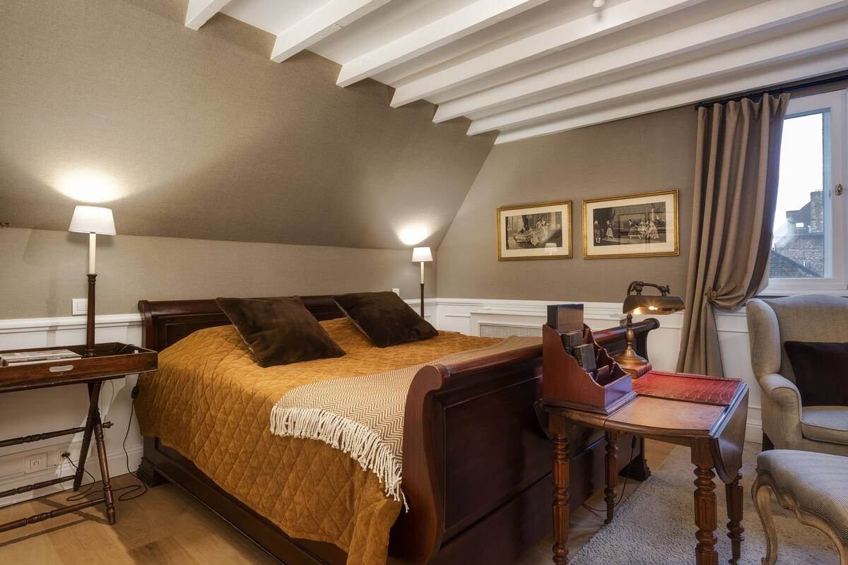 Un dormitorio con cama, mesitas de noche, escritorio y una silla. Hay dos cuadros en la pared.