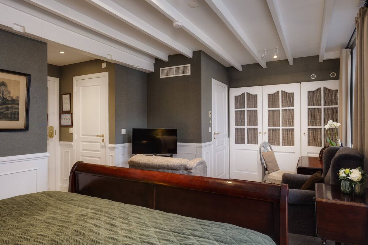 Un dormitorio con cama, televisión, una silla y ventana con vistas al exterior.