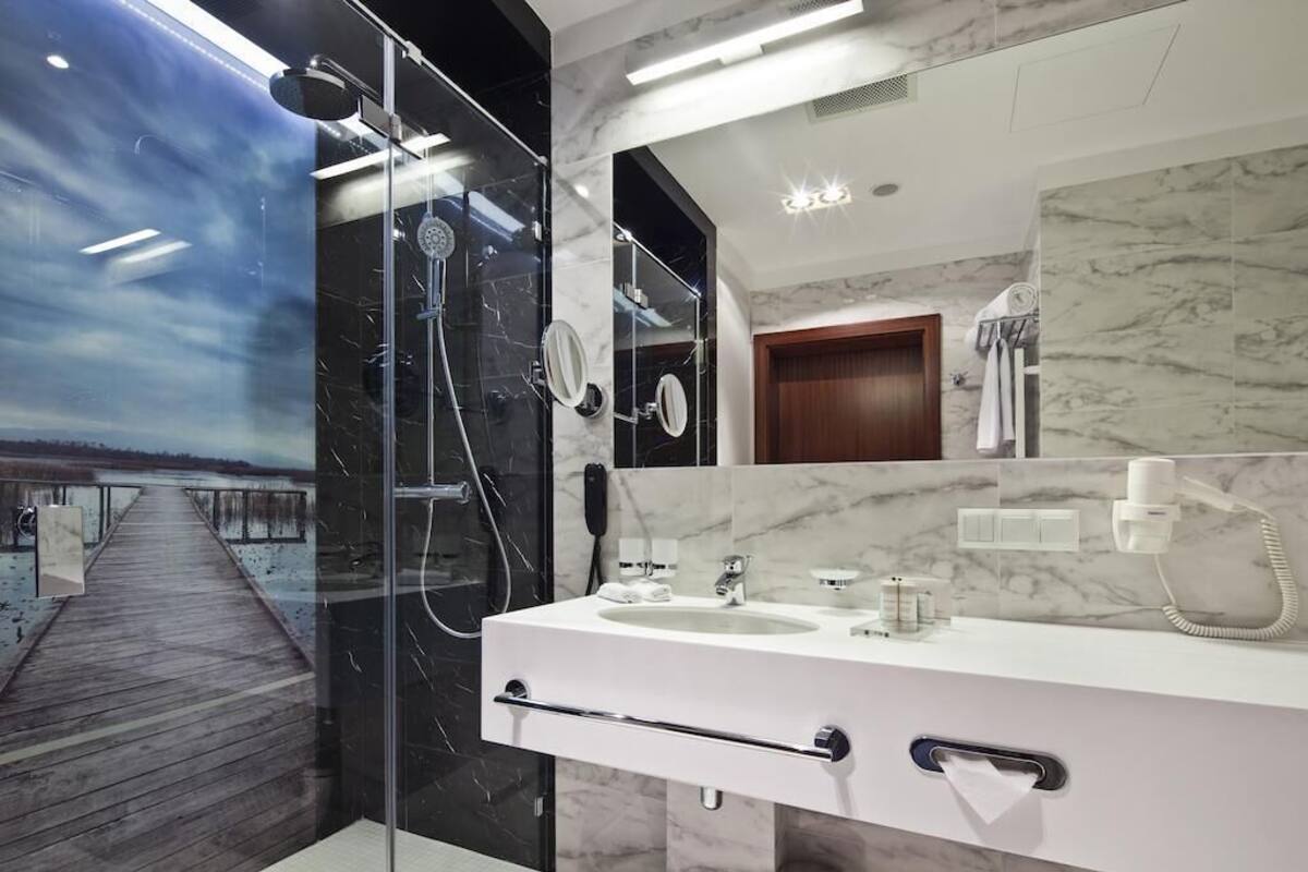 Une salle de bain moderne avec une douche à parois de verre, un meuble-lavabo en marbre et un grand miroir.