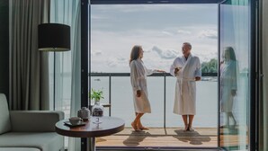 A modern room with a sofa, a table with a teapot and cup, and a balcony with a view of the water. - Hotel Mikołajki Leisure & SPA - Destigo Hotels (Mikolajki)
