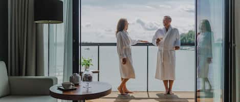 A modern room with a sofa, a table with a teapot and cup, and a balcony with a view of the water.