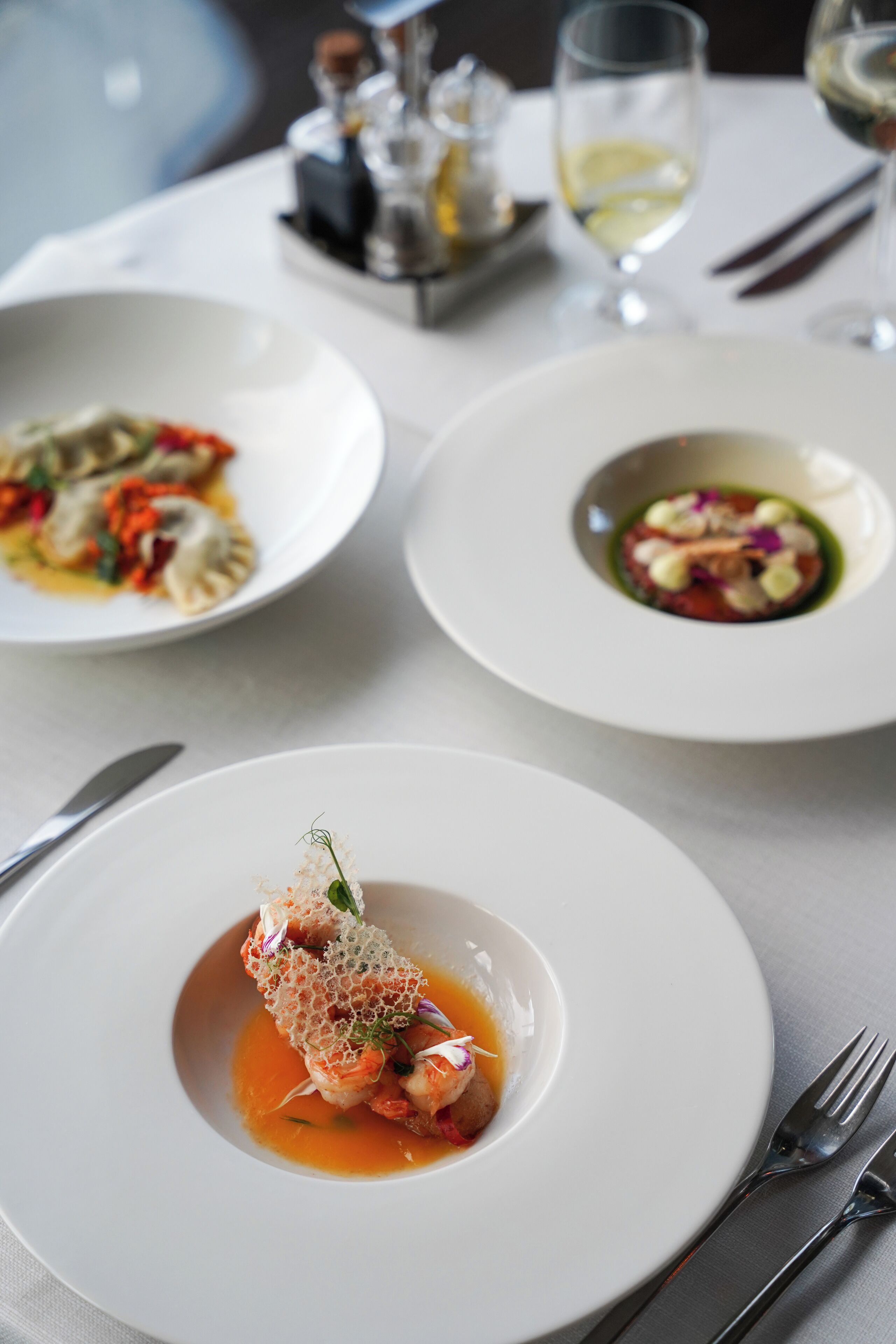 A dining table with three white plates of food, each with a different dish.