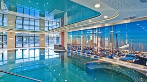 A large indoor swimming pool with a glass wall displaying sailboats. - Hotel Mikołajki Leisure & SPA - Destigo Hotels (Mikolajki)