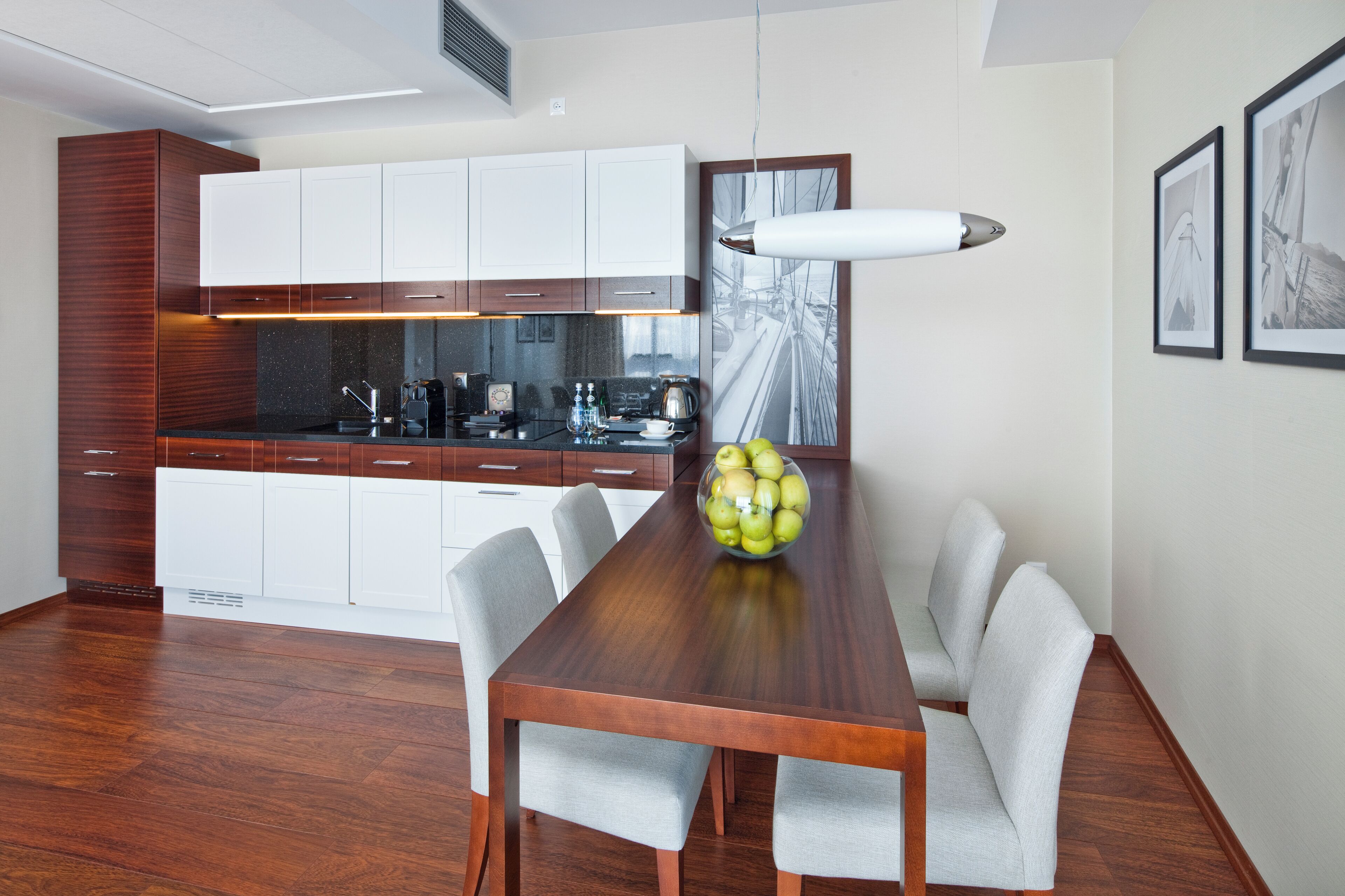 Een moderne keuken met witte kasten, een houten eettafel en een schaal fruit.