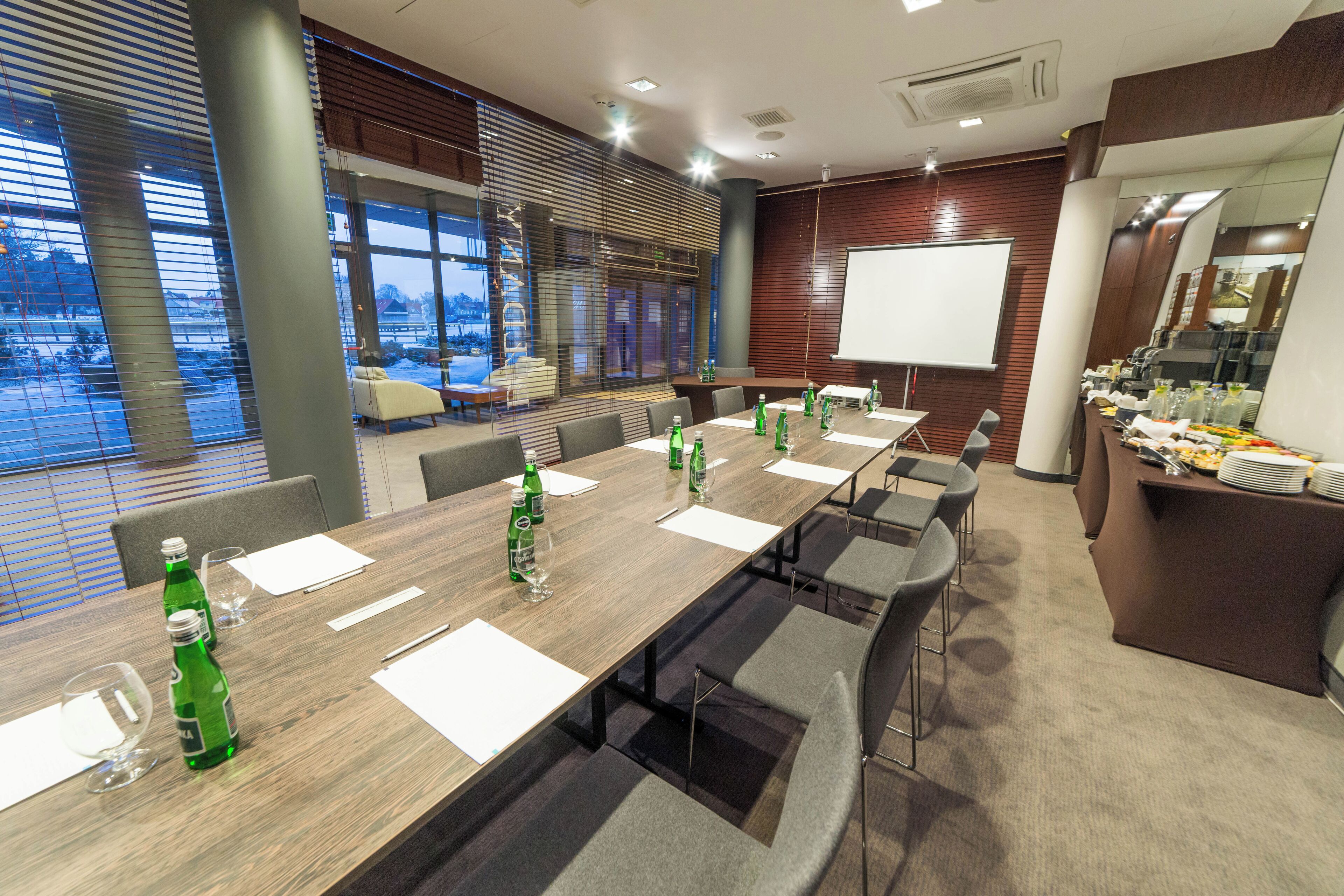 A conference room with a long table, chairs, a whiteboard, and a buffet area.