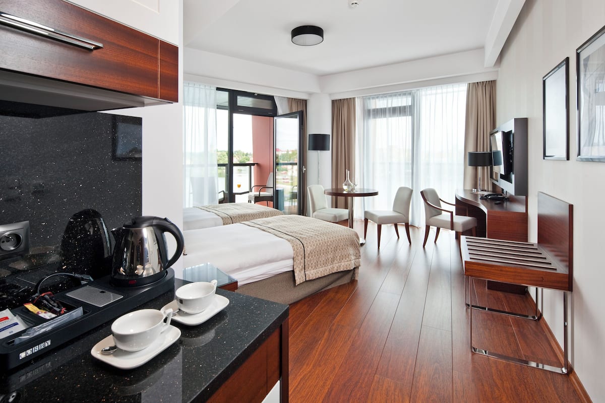 Een moderne hotelkamer met een bed, een bureau met stoel, een kleine tafel met stoelen, een televisie en een balkon met uitzicht.