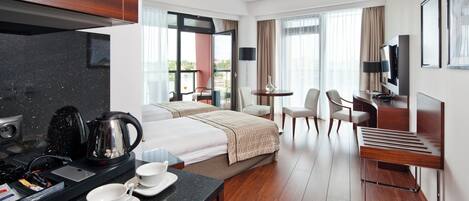 Una habitación de hotel moderna con cama, escritorio y silla, una pequeña mesa con sillas, televisión y balcón con vistas.