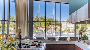 A dining area with a view of a marina, large windows, and a buffet setup. - Hotel Mikołajki Leisure & SPA - Destigo Hotels (Mikolajki)