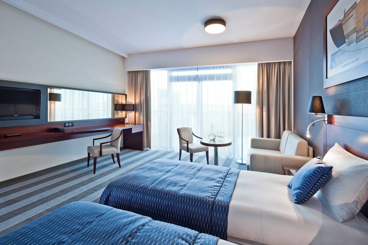 Een hotelkamer met een bed, bureau, stoel, televisie en een raam met gordijnen.