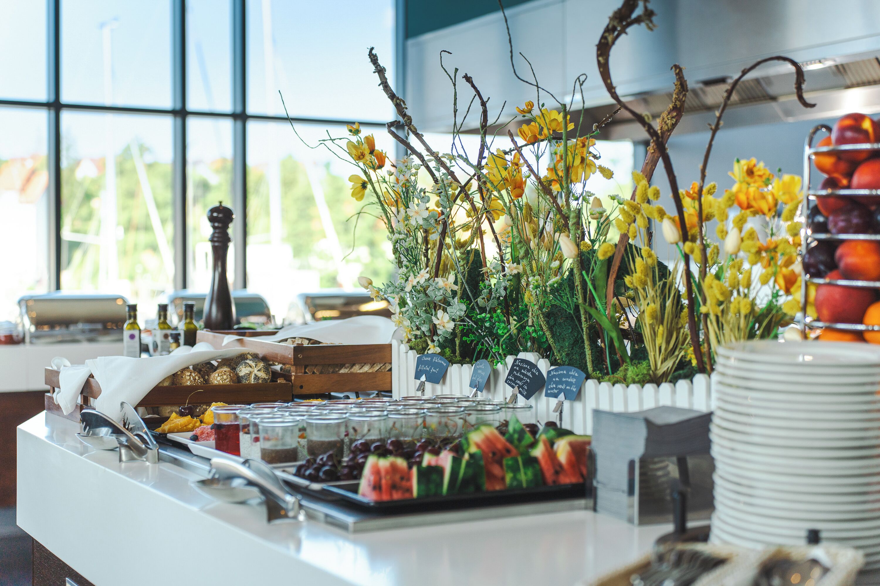 Mesa de buffet con diversos alimentos, un arreglo floral decorativo y una presentación de frutas.