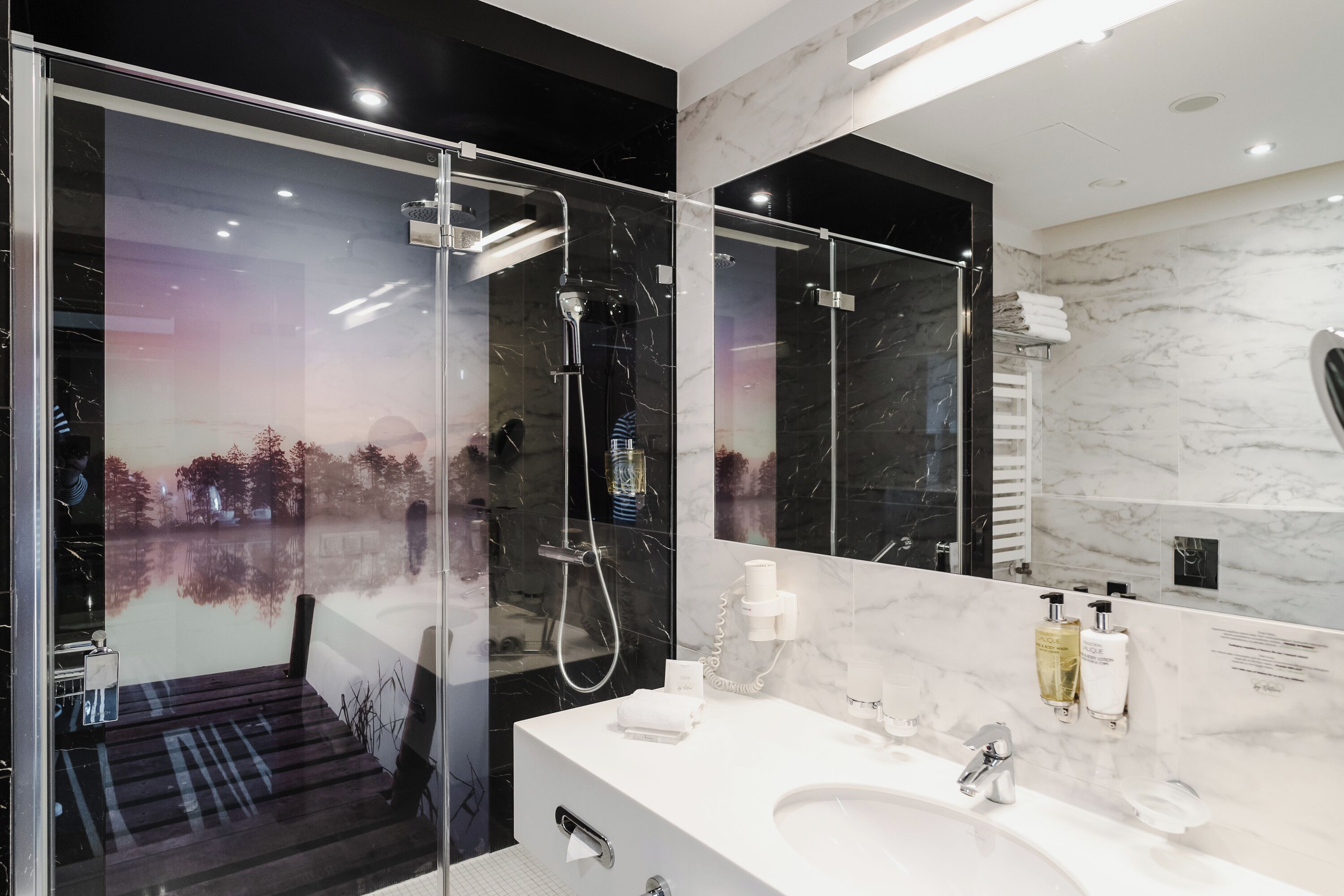 A modern bathroom with a glass-enclosed shower, a large mirror, and a white marble countertop.