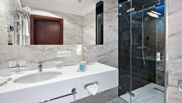 A modern bathroom with a marble sink, a glass shower enclosure, and a wooden door.