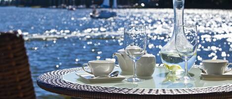 A table with tea set and glasses by a lake with boats in the background.
