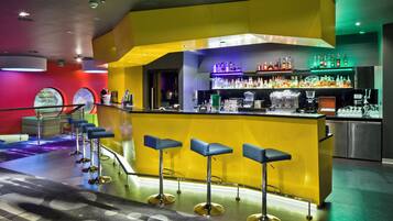 Una zona de bar con un mostrador amarillo, varios taburetes y una gran variedad de botellas y vasos.