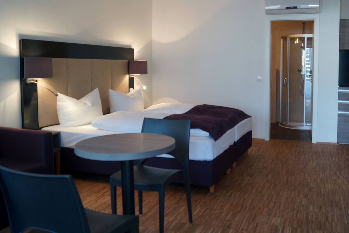 A modern hotel room with a bed, a round table, and a TV.