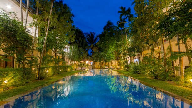 A swimming pool surrounded by lush greenery and palm trees, with a well-lit deck area. - La Residence WatBo Hotel (Siem Reap)