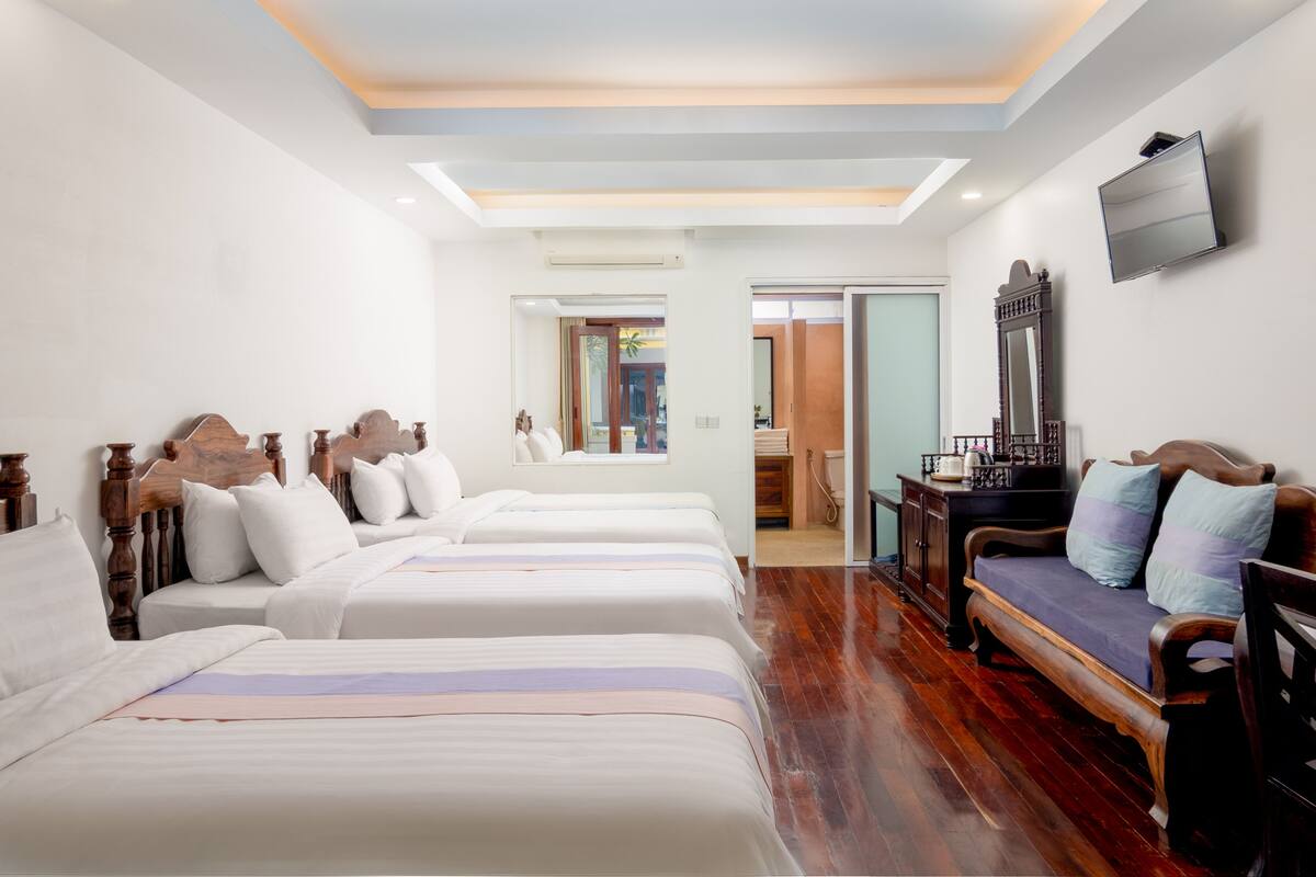 A hotel room with three beds, a wooden bench, a television, and a mirror.