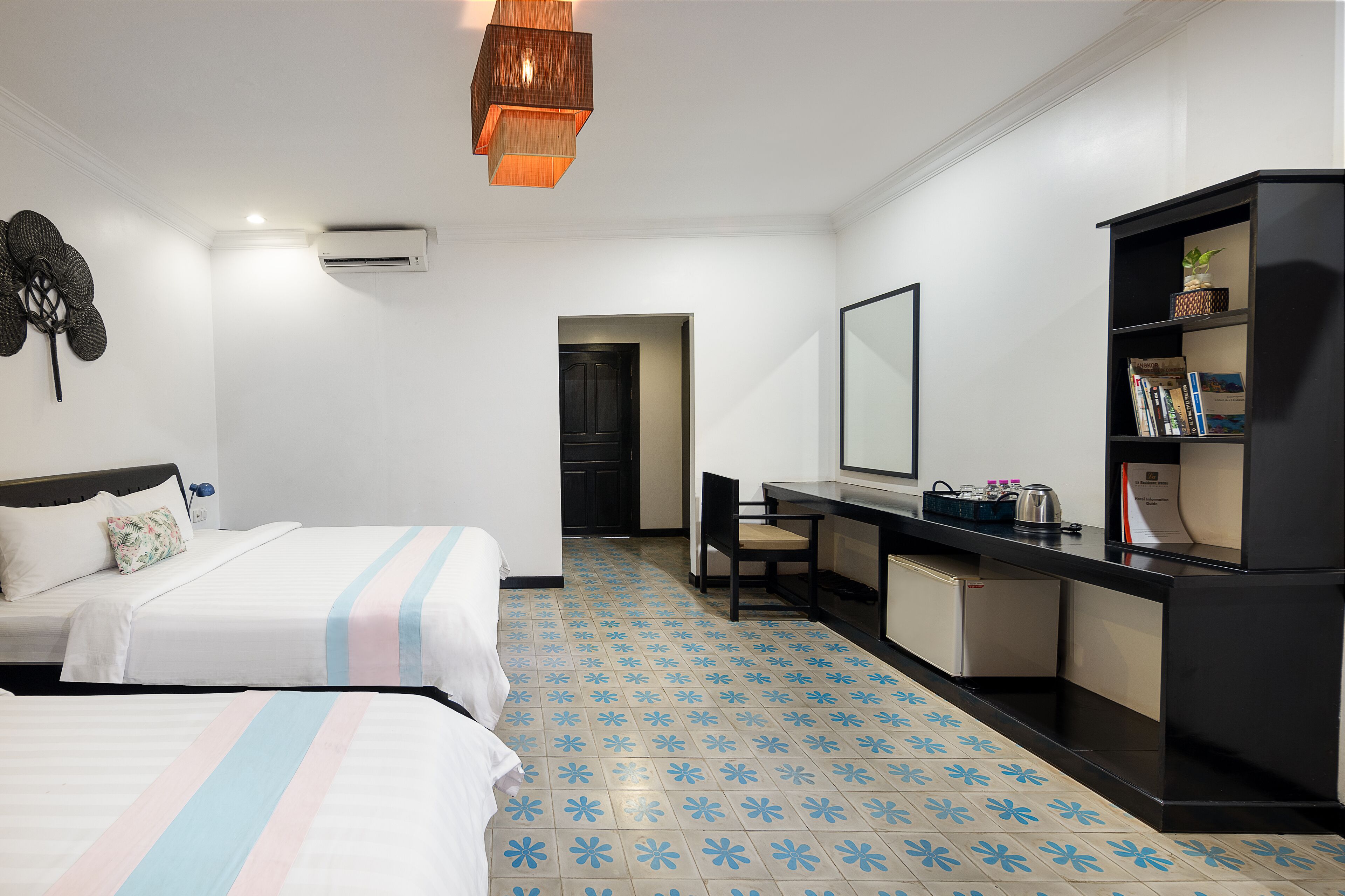 A hotel room with two beds, a desk, a bookshelf, and a bathroom visible through an open door.