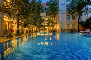 A large indoor swimming pool with tiled blue floor, surrounded by lush greenery and a building with classical architecture in the background. - La Residence WatBo Hotel (Siem Reap)
