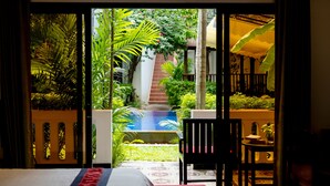 A bedroom with a bed, a chair, and a view of a pool and garden. - La Residence WatBo Hotel (Siem Reap)