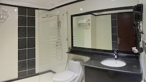 A modern bathroom with a glass-enclosed shower, a white toilet, a black vanity with a sink, and a large mirror. - Concorde Mina Hotel (Makkah)