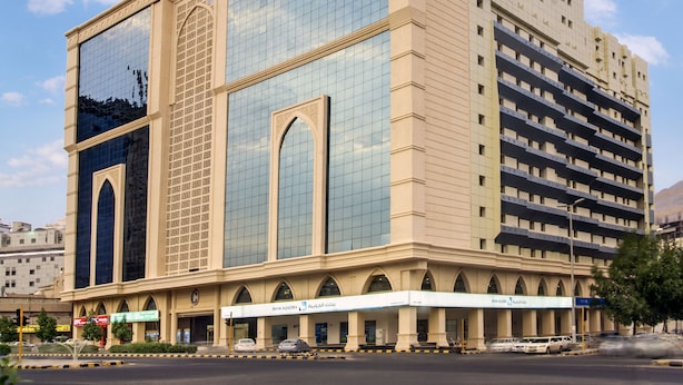 A multi-story hotel with a modern glass facade, a central entrance with arched doorways, and a series of balconies on the upper floors. - Concorde Mina Hotel (Makkah)