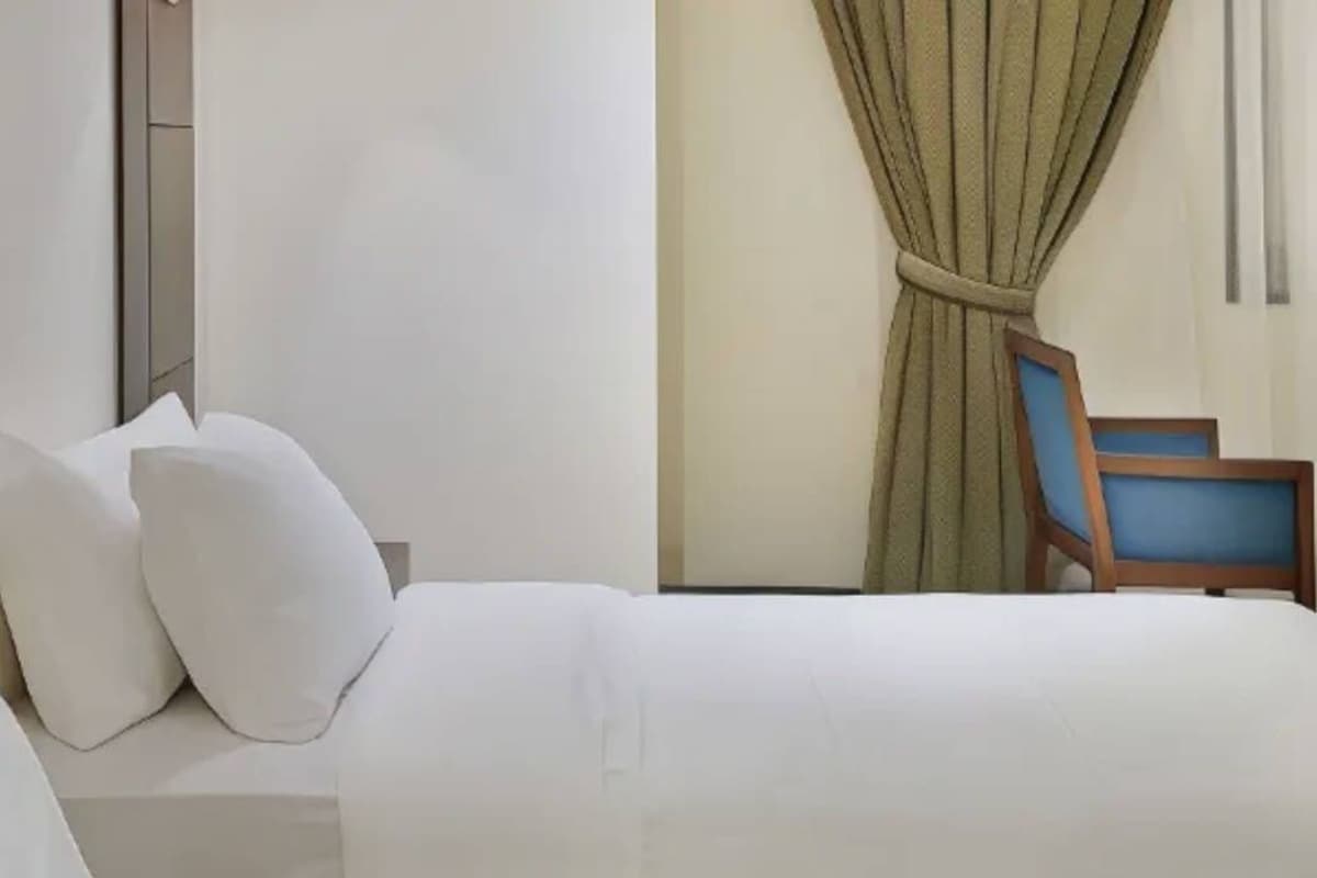 Une chambre d’hôtel avec un lit, des oreillers, une chaise et un rideau.