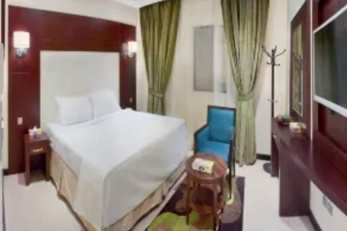 Une chambre d’hôtel avec un grand lit, une petite table ronde, un fauteuil bleu et un téléviseur.